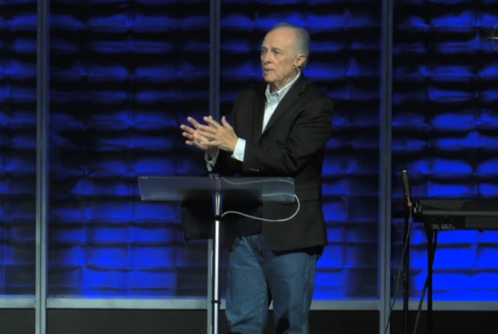 Dr. Mark Rutland is standing at a podium with his hands folded