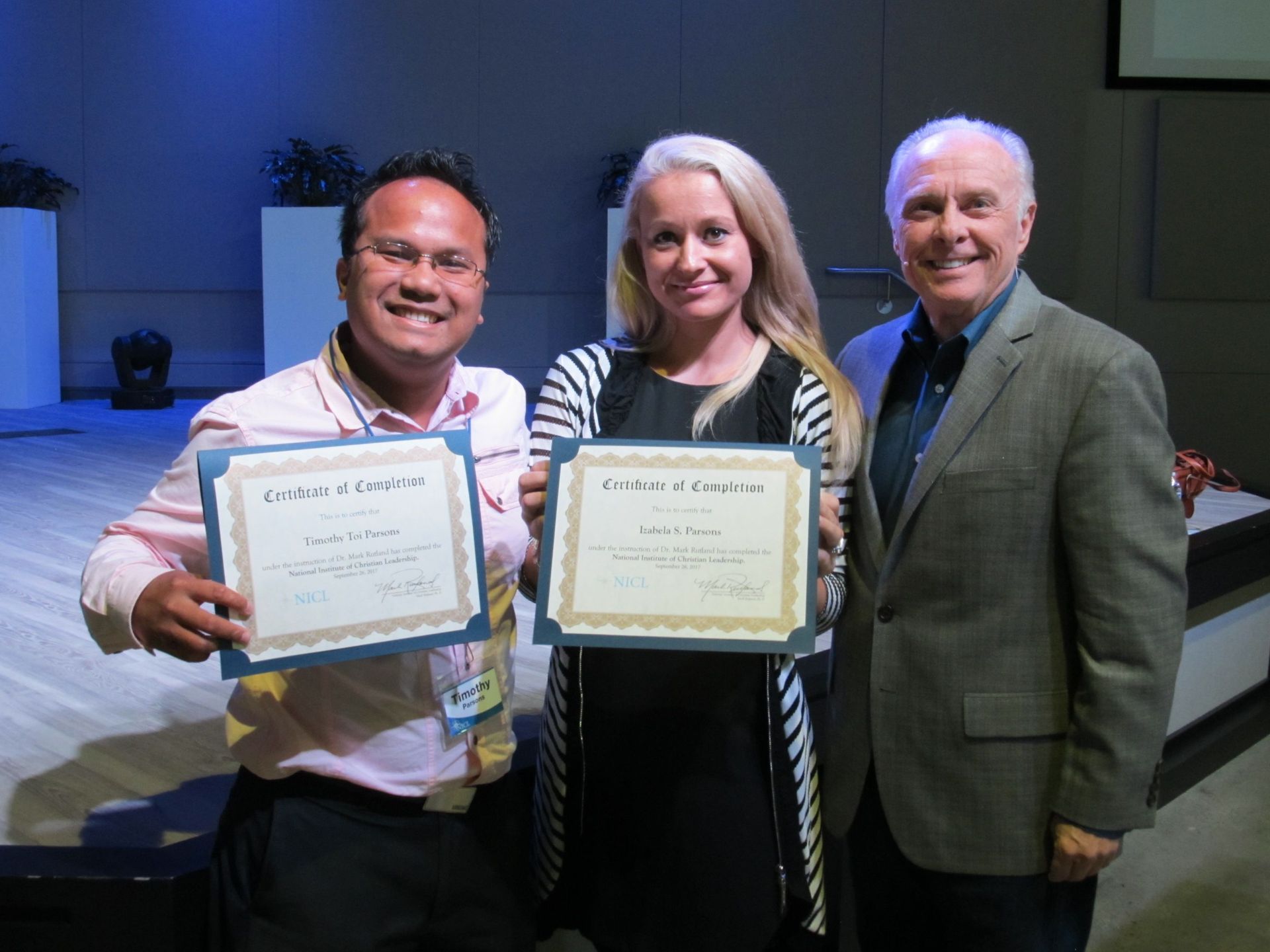 Dr. Mark Rutland standing with two graduates holding certificates in their hands