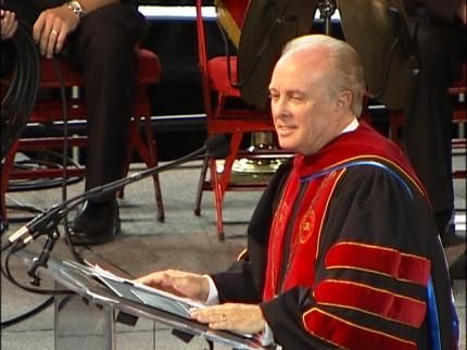 Dr. Mark Rutland  in a graduation gown is sitting at a podium