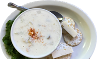 Clam chowder in white bowl with crackers and cheese on a plate.