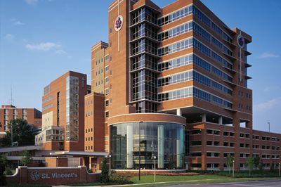 Modern brick hospital building with glass entrance and a sign in front, under a clear blue sky
