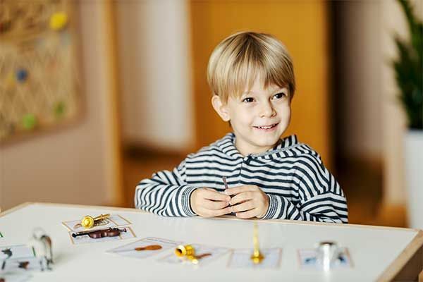 Blond child in striped shirt smiling at a table with small toy cars