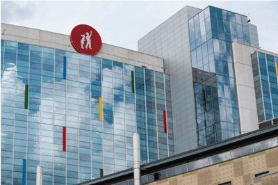 Modern glass hospital building with red medical logo and colorful vertical accents