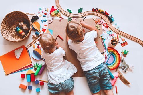 Two children playing with colorful toys and craft supplies on a white table