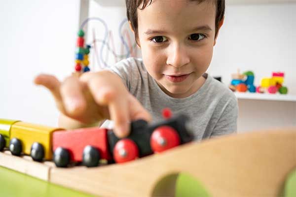Child reaching toward a toy train on a wooden track indoors