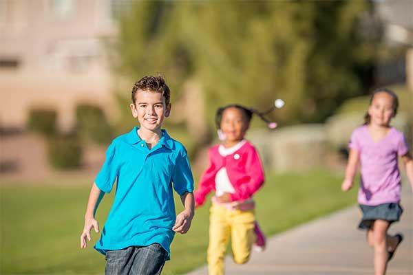 Children running on a sunny sidewalk, with one boy in a blue shirt in the foreground