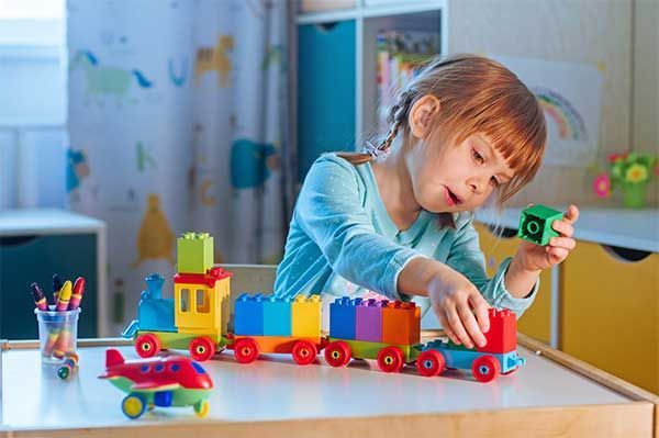 Child playing with colorful toy train at a table in a bright playroom