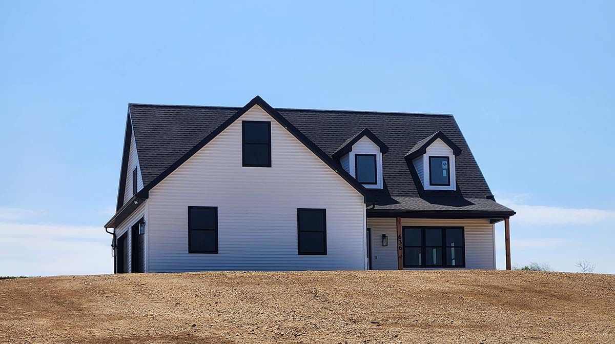 A white house with a black roof is sitting on top of a dirt hill.