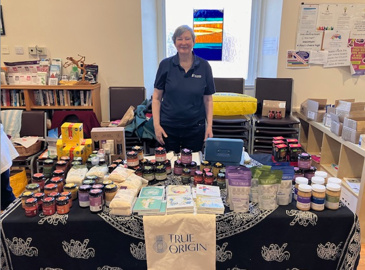 A woman standing at  church fair trade stall with lots of delicious fair trade products available