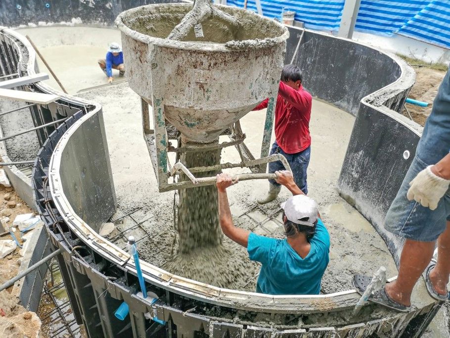 Workers mixing concrete in a large circular tank at a construction site