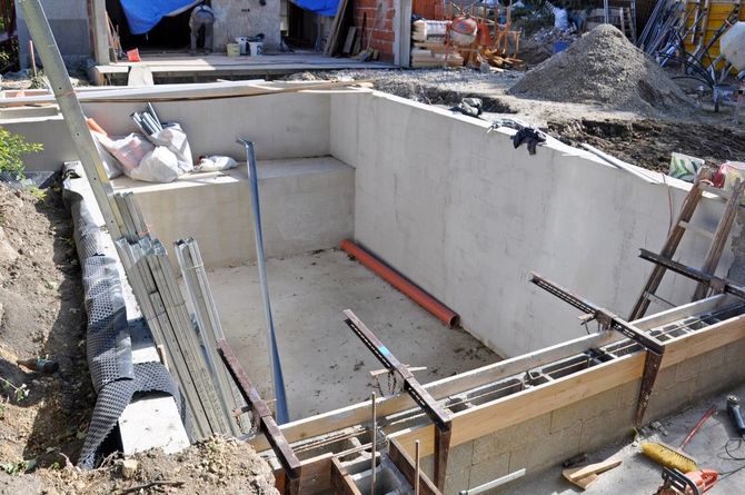 Concrete foundation under construction with ladder, rebar, and tools in a dug-out site.