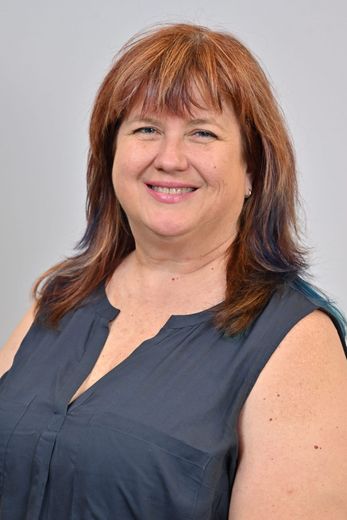 Smiling woman with auburn hair in a navy sleeveless blouse against a light gray background