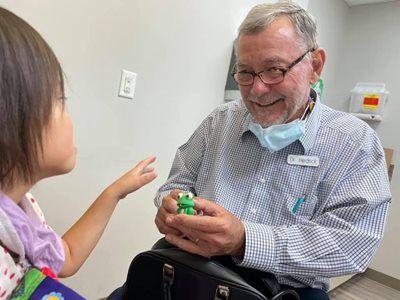 Doctor shows a toy frog to a child in an office setting. Both are smiling, the doctor is holding the toy.