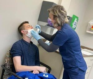 Medical professional administering a medical test to a seated person. Both wear face masks.