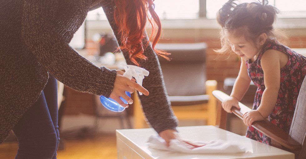 A woman and a little girl are cleaning a table in a living room.