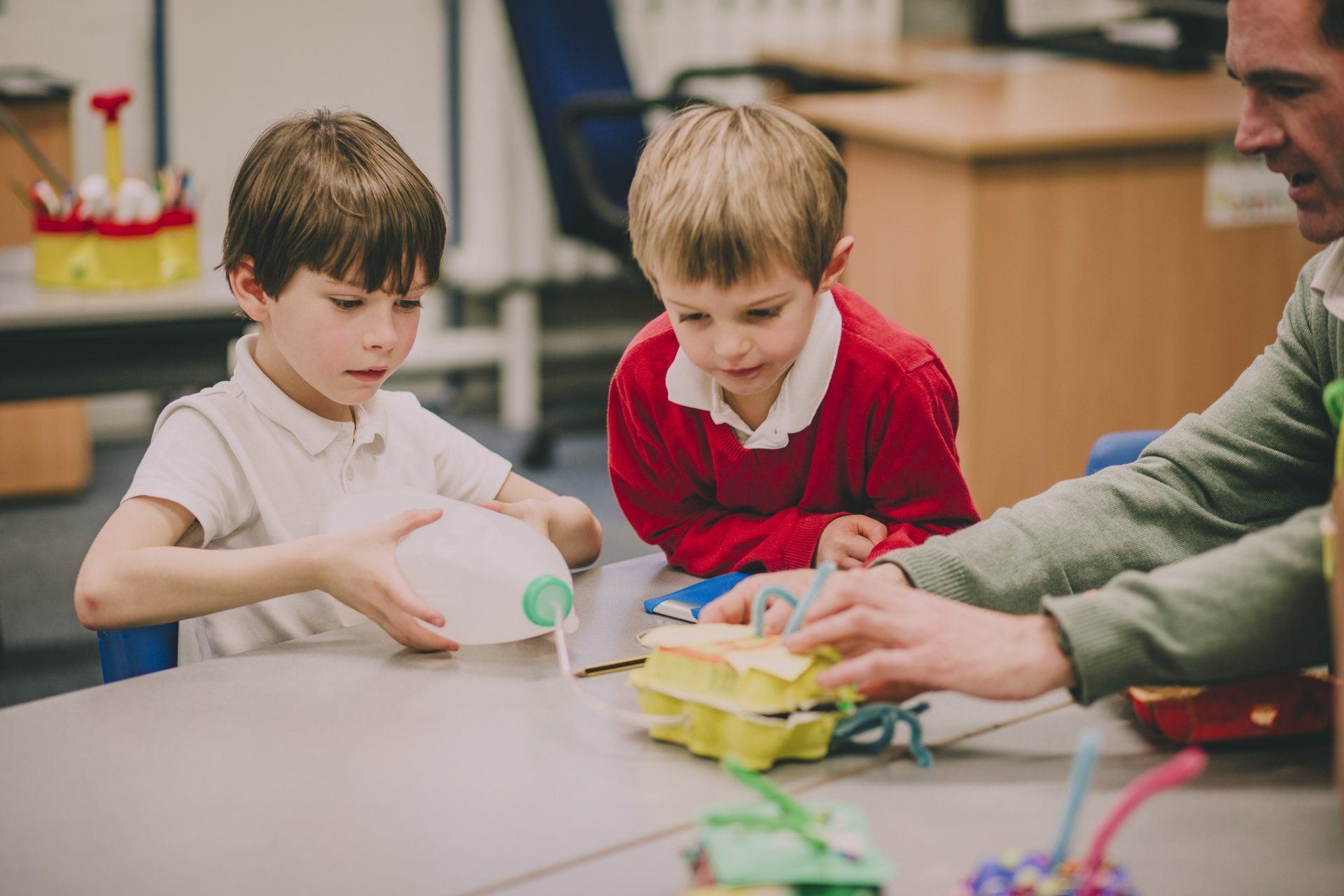 A group of young boys are sitting at a table playing with toys.