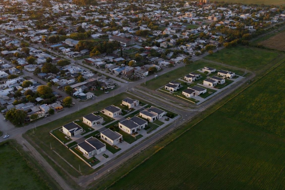 Vista aérea de un barrio residencial con hileras de casas junto a un gran campo verde al atardecer.