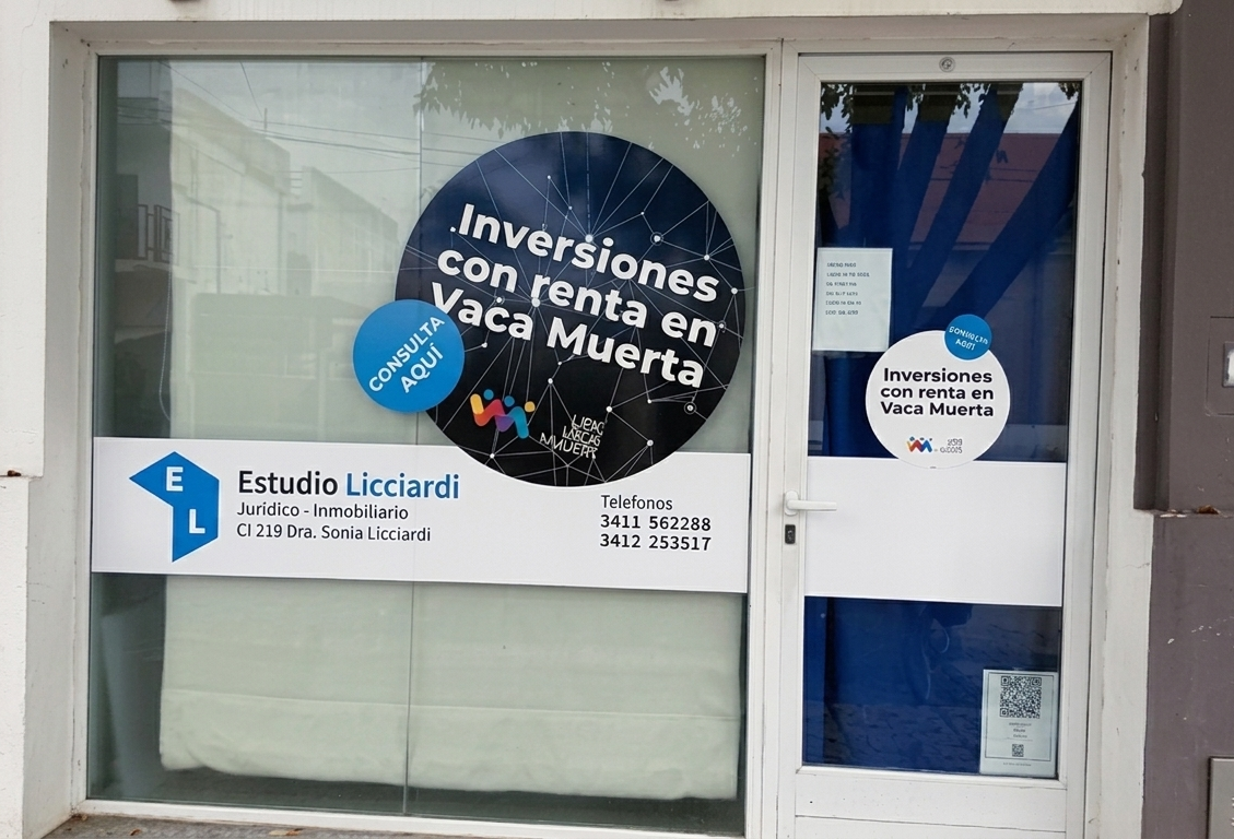 Cuaderno abierto, papeles y bolígrafos sobre un escritorio de madera junto a una cartera negra cerca de una ventana.
