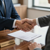 Dos personas se dan la mano sobre un escritorio, con un documento de contrato de compraventa y un mazo de juez a la vista.