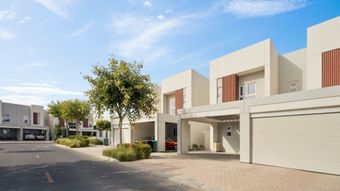 Hilera de casas adosadas modernas con aparcamiento cubierto, pequeños árboles y un cielo azul despejado.