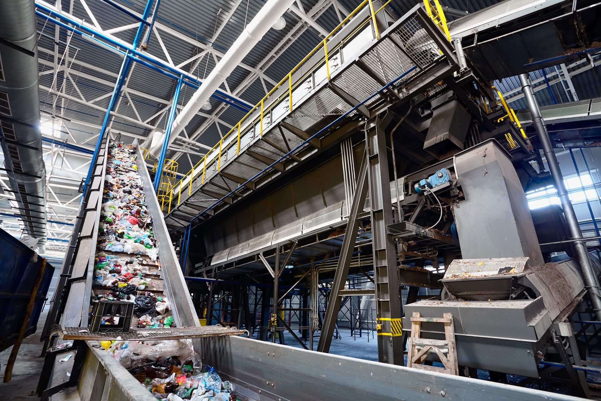 Recycling plant interior with conveyor belt of mixed waste, industrial machinery.