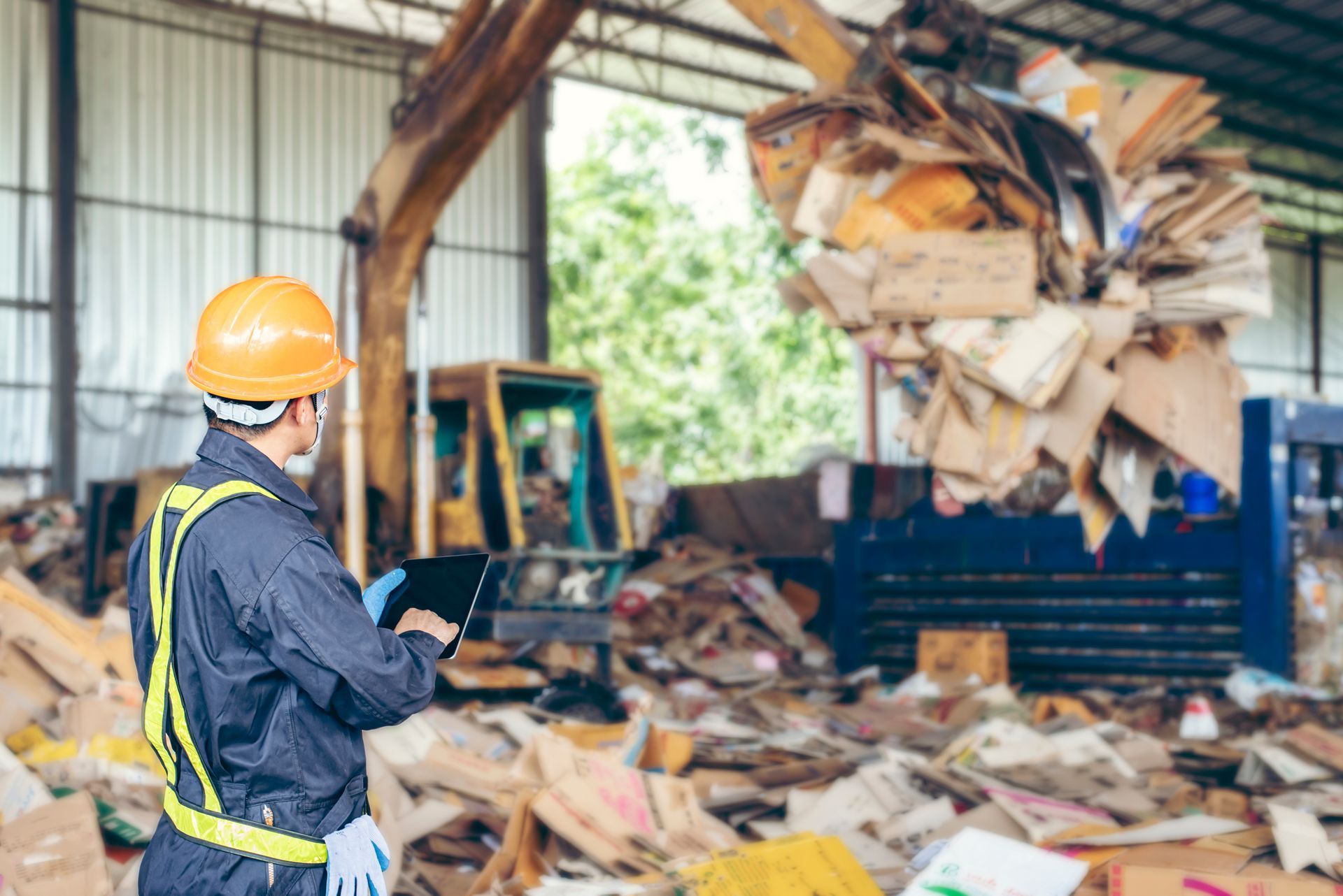 Worker in safety gear inspects recycling pile with tablet, excavator in background. Worker in safety gear inspects recycling pile with tablet, excavator in background.