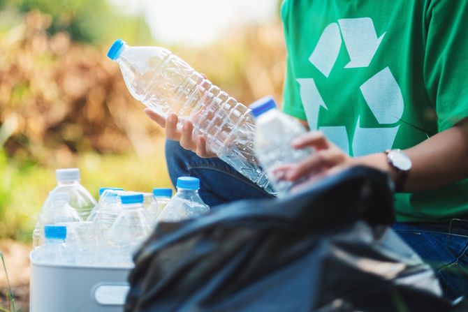Person in green shirt with recycling symbol collecting plastic water bottles. Person in green shirt with recycling symbol collecting plastic water bottles.
