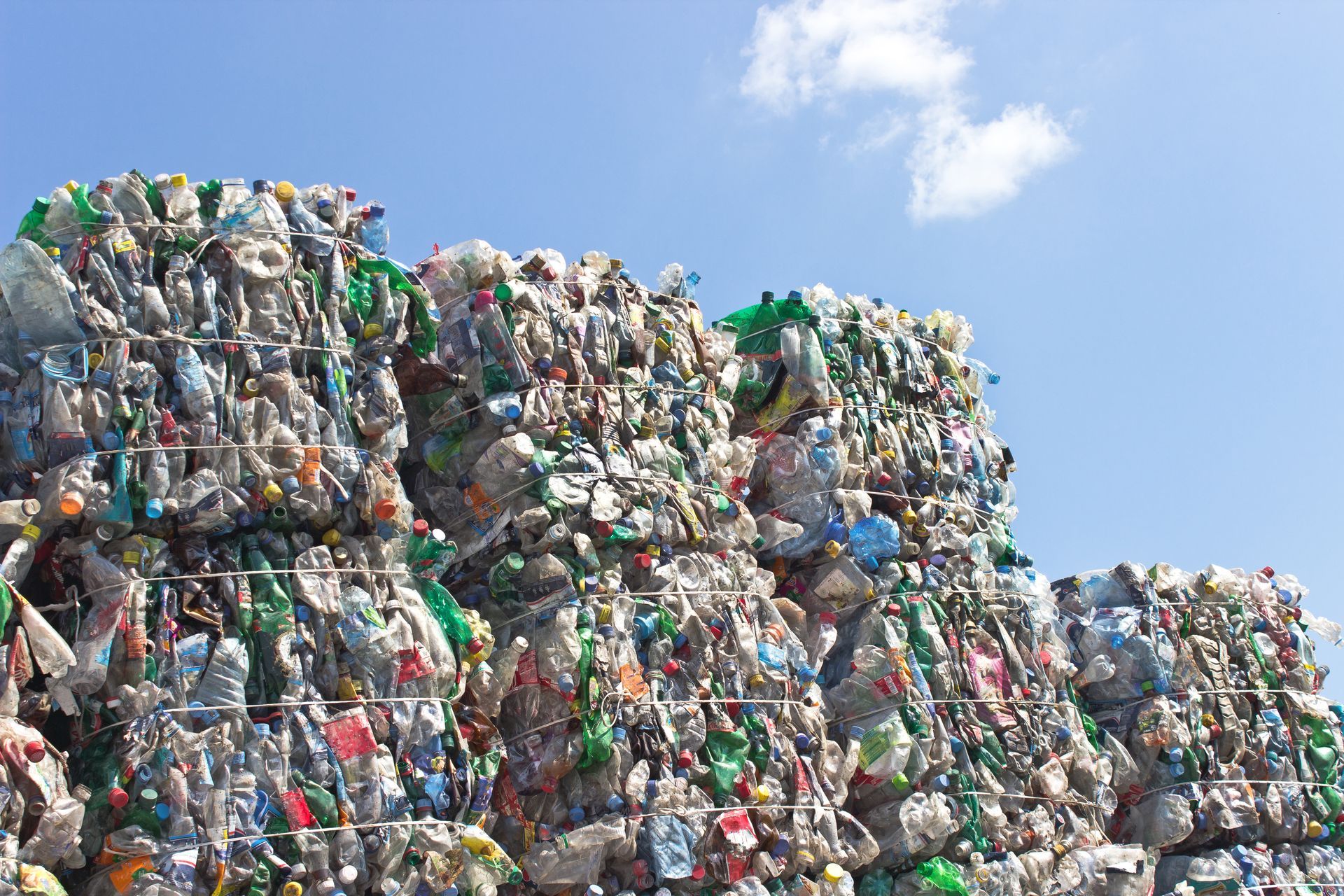 Large stack of compressed plastic bottles against a blue sky.