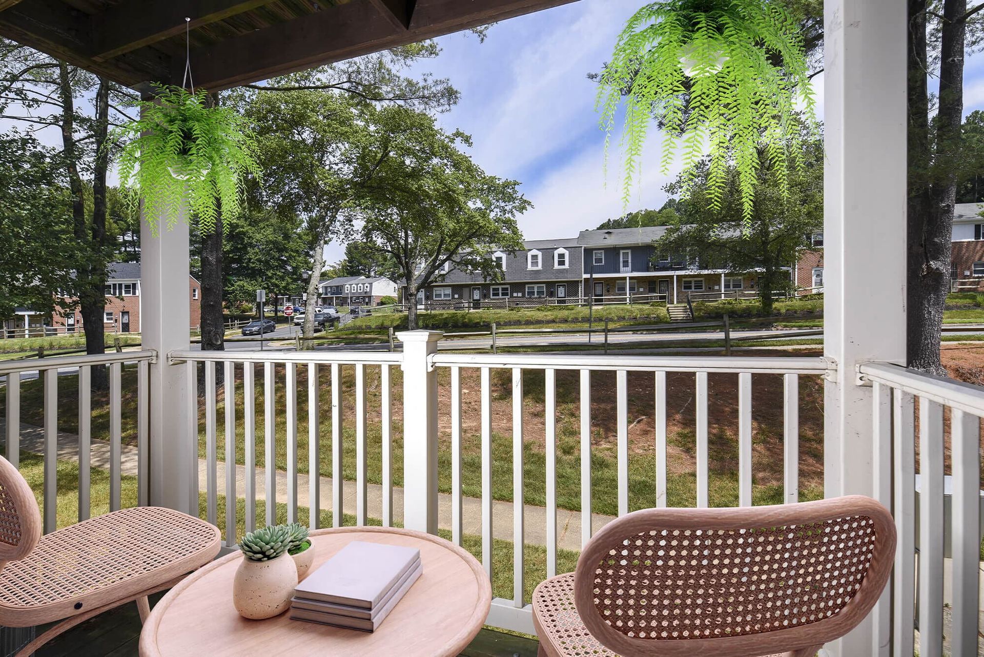 Balcony with white railing and wicker chairs, overlooking a tree-lined apartment complex.