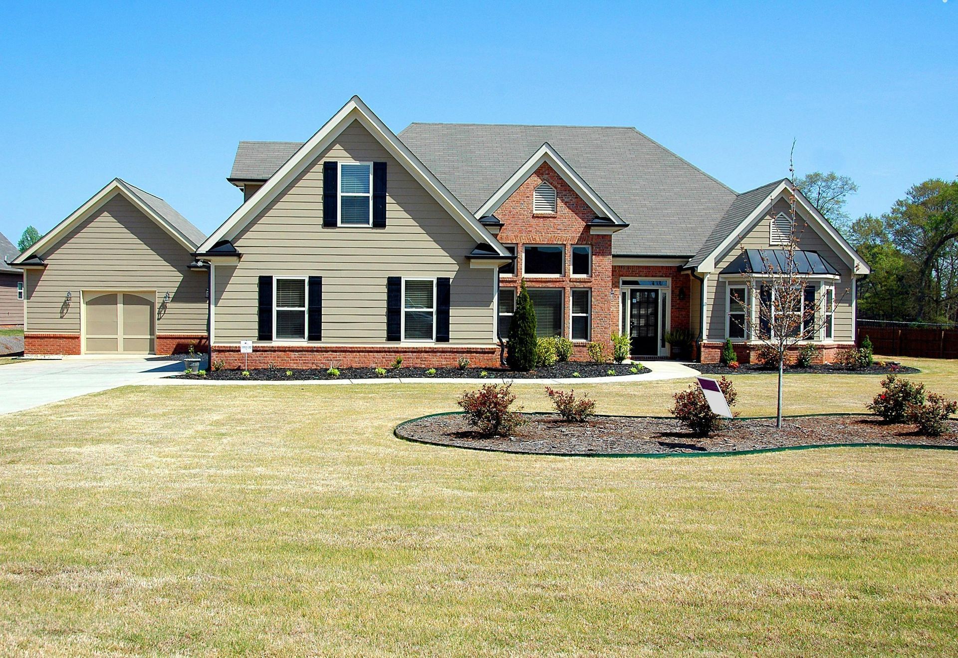 House with tan siding, brick accents, and a garage on a sunny day.