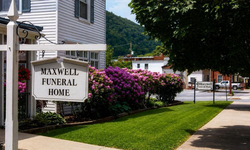 Maxwell Funeral Home sign at Lock Haven, PA Funeral Home and Cremations with pink shrubs and hillside backdrop