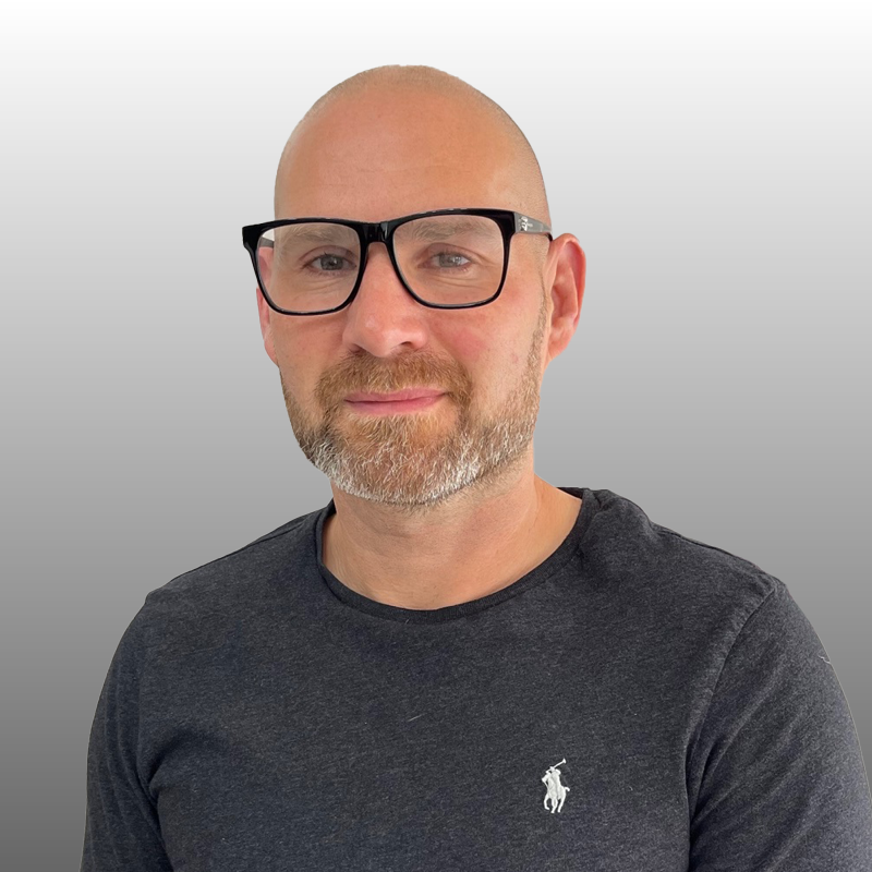 Portrait of a bald man with glasses and a grey shirt, standing against a light background. Freehold management service. Freehold manager.