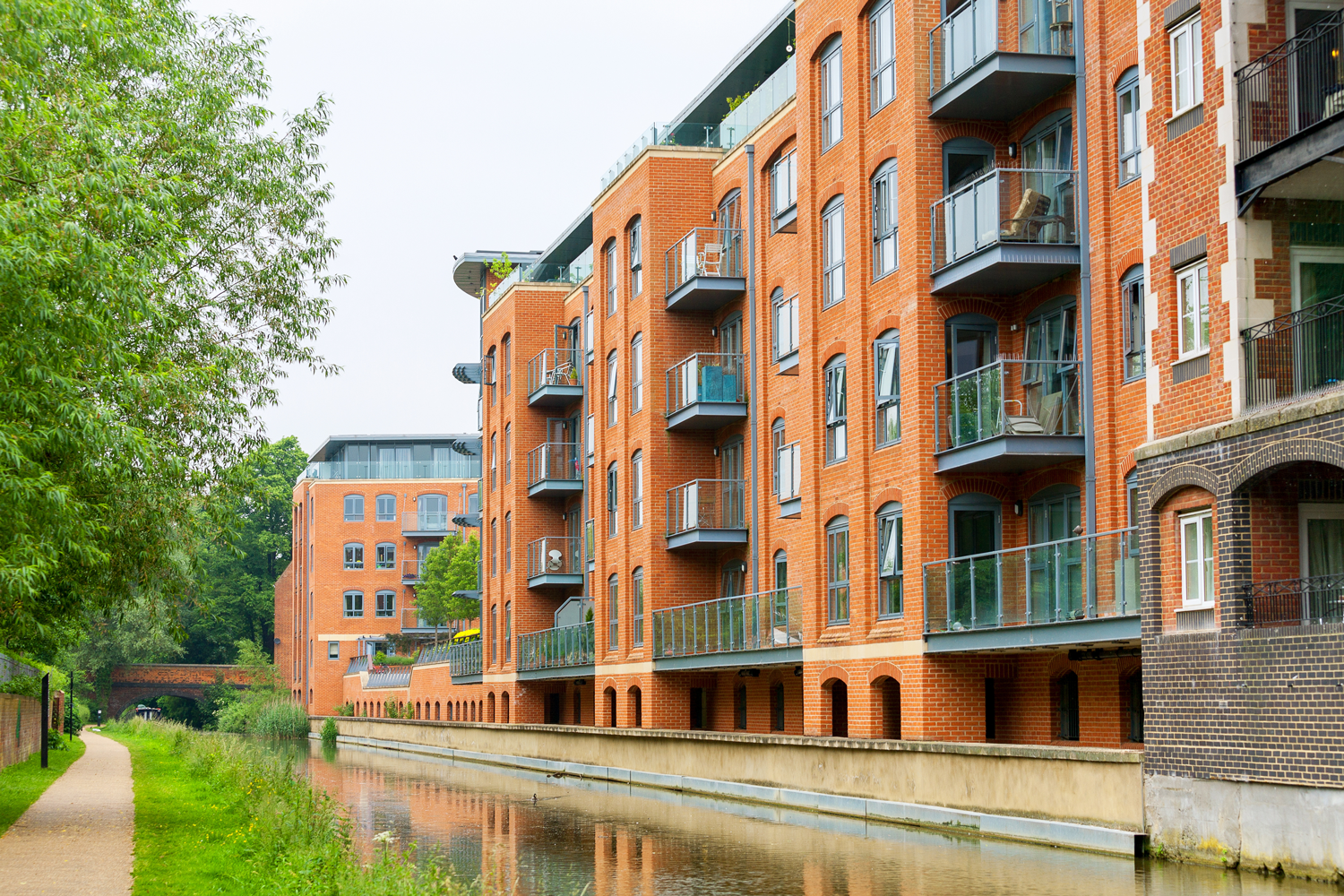Brick apartment buildings along a canal beside a tree-lined path. Freehold management service. Freehold manager.