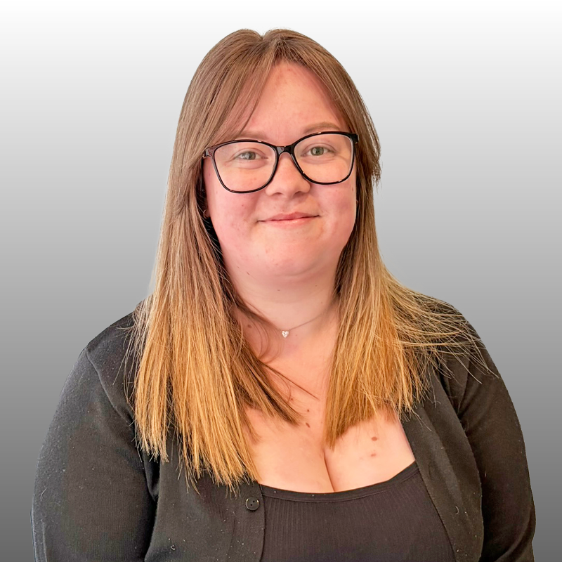 Person with glasses and long hair smiling against a light grey background. Freehold management service. Freehold manager.