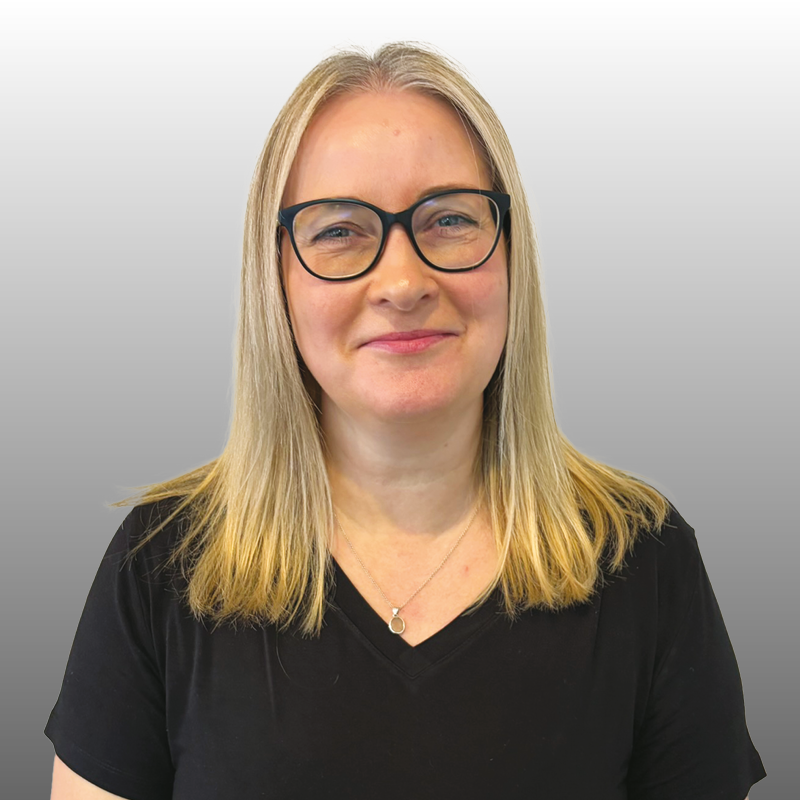 Smiling woman with blonde hair and glasses wearing a black top against a plain grey background. Freehold management service. Freehold manager.