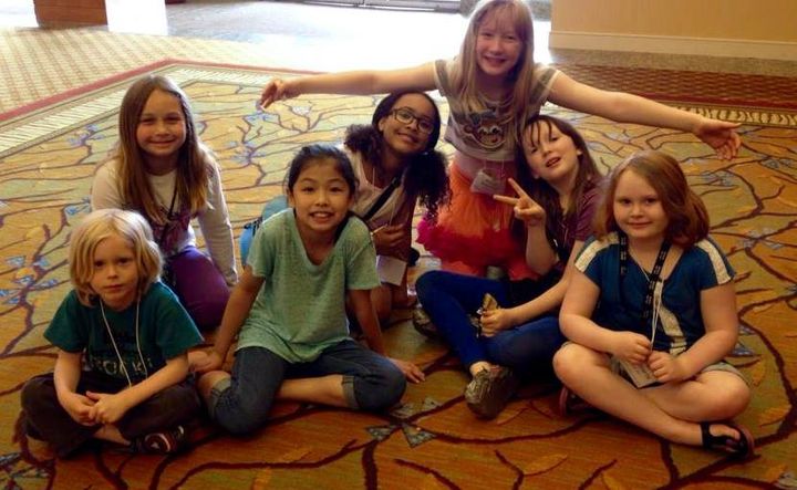 A group of young girls are sitting on the floor posing for a picture.