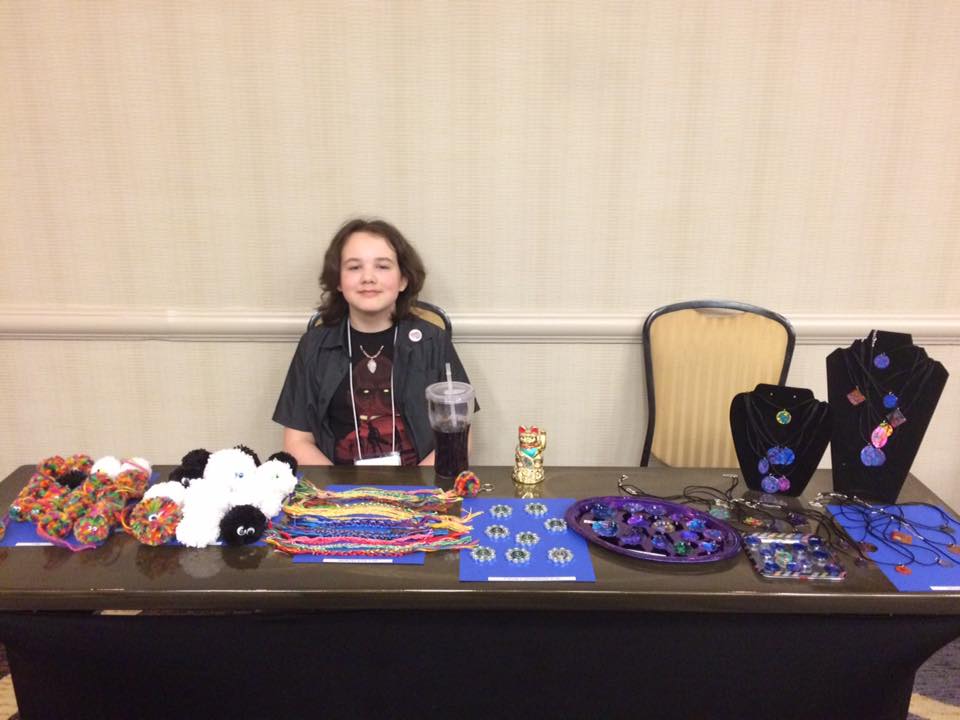 A young girl is sitting at a table with jewelry on it.