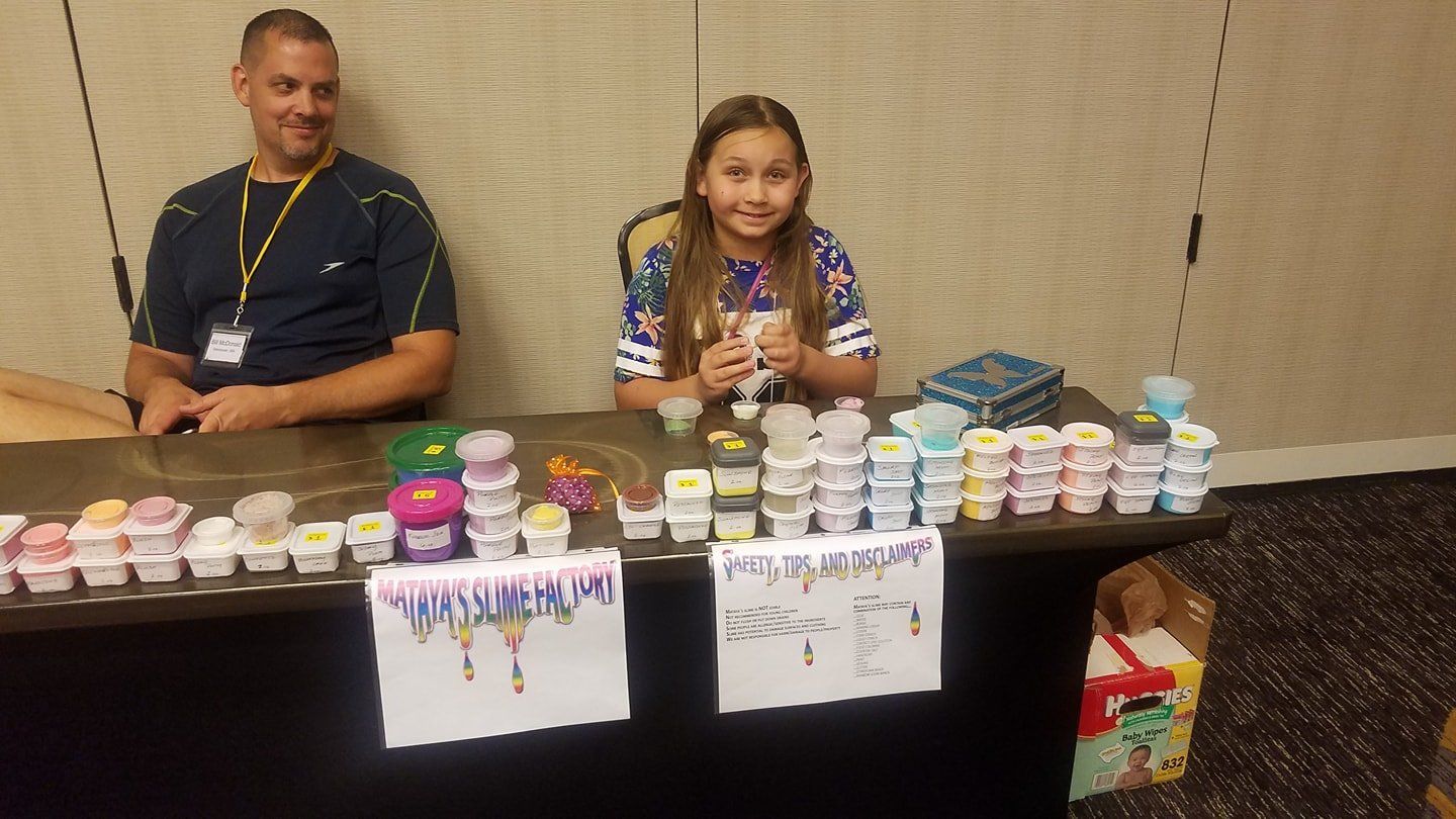 A man and a girl are sitting at a table selling slime.