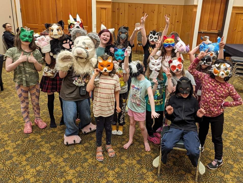 A large group of happy children wearing playful animal masks, having fun and embracing creativity at a LIFE is Good Unschooling Conference funshop.