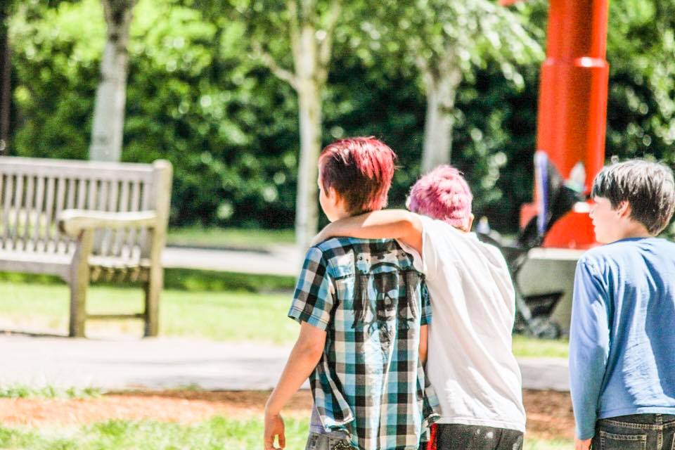 Three young boys are walking in a park with their arms around each other.