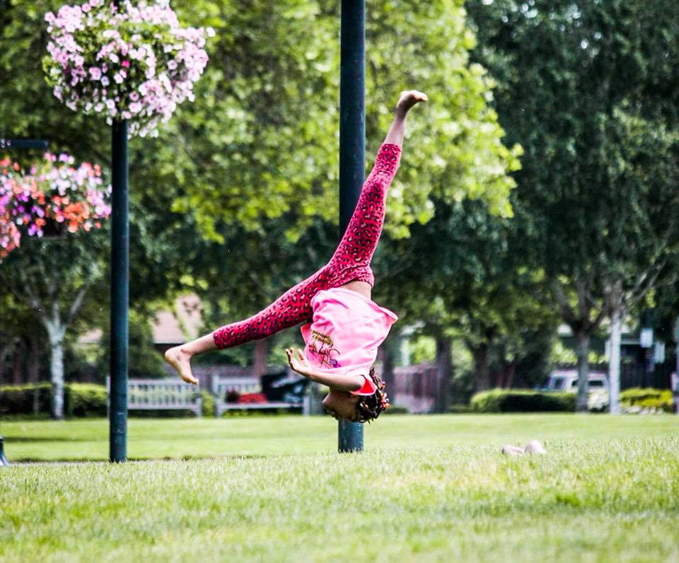 A young girl is doing a handstand in a park.
