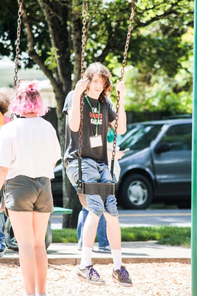 A girl with pink hair is sitting on a swing at a playground.
