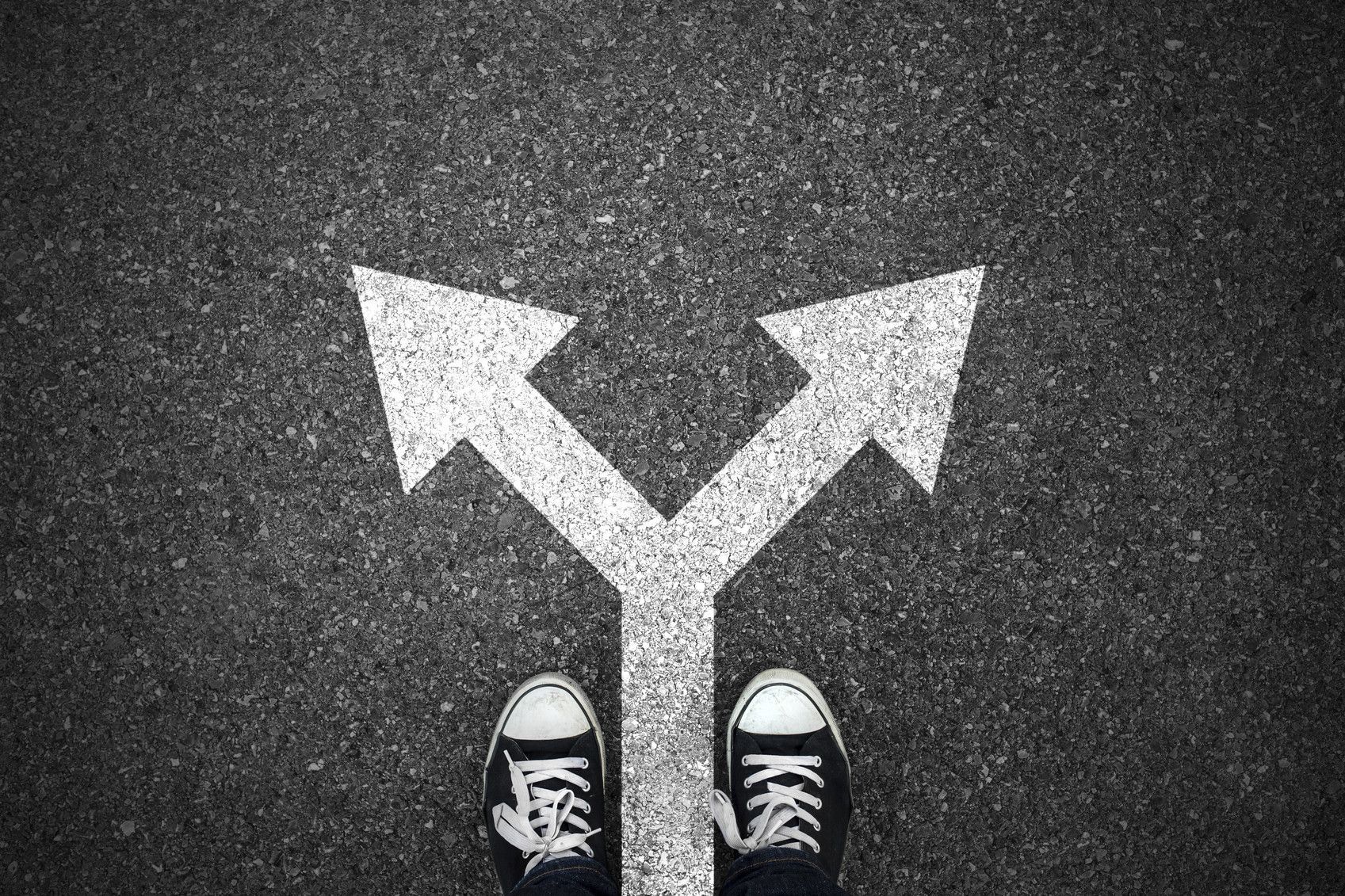 Shoes on pavement facing a painted forked arrow showing two possible directions.