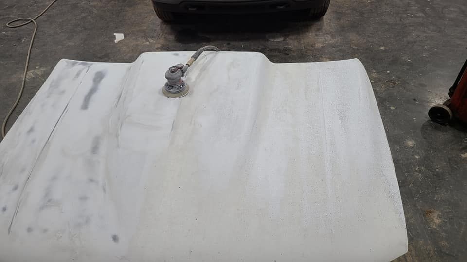 A white hood is sitting on the ground next to a car.