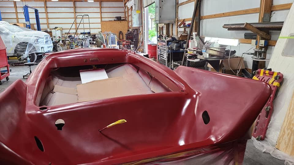 A red boat is sitting in a garage being painted.