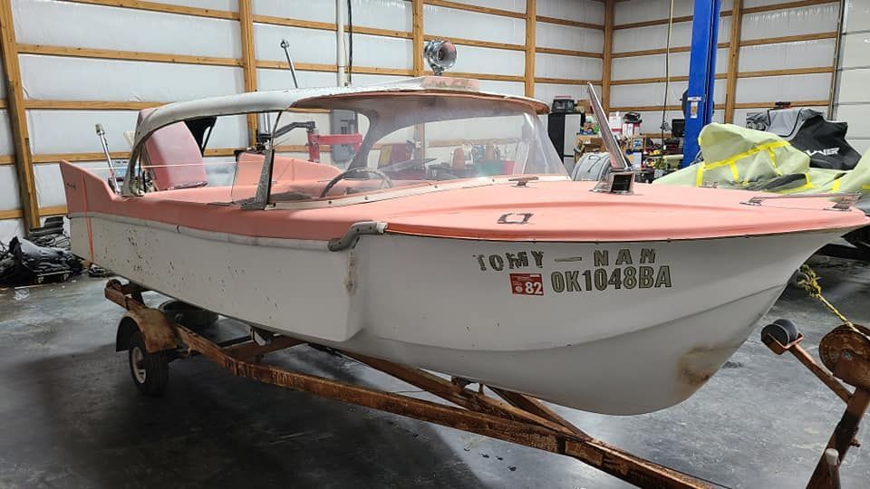 A pink and white boat is on a trailer in a garage.