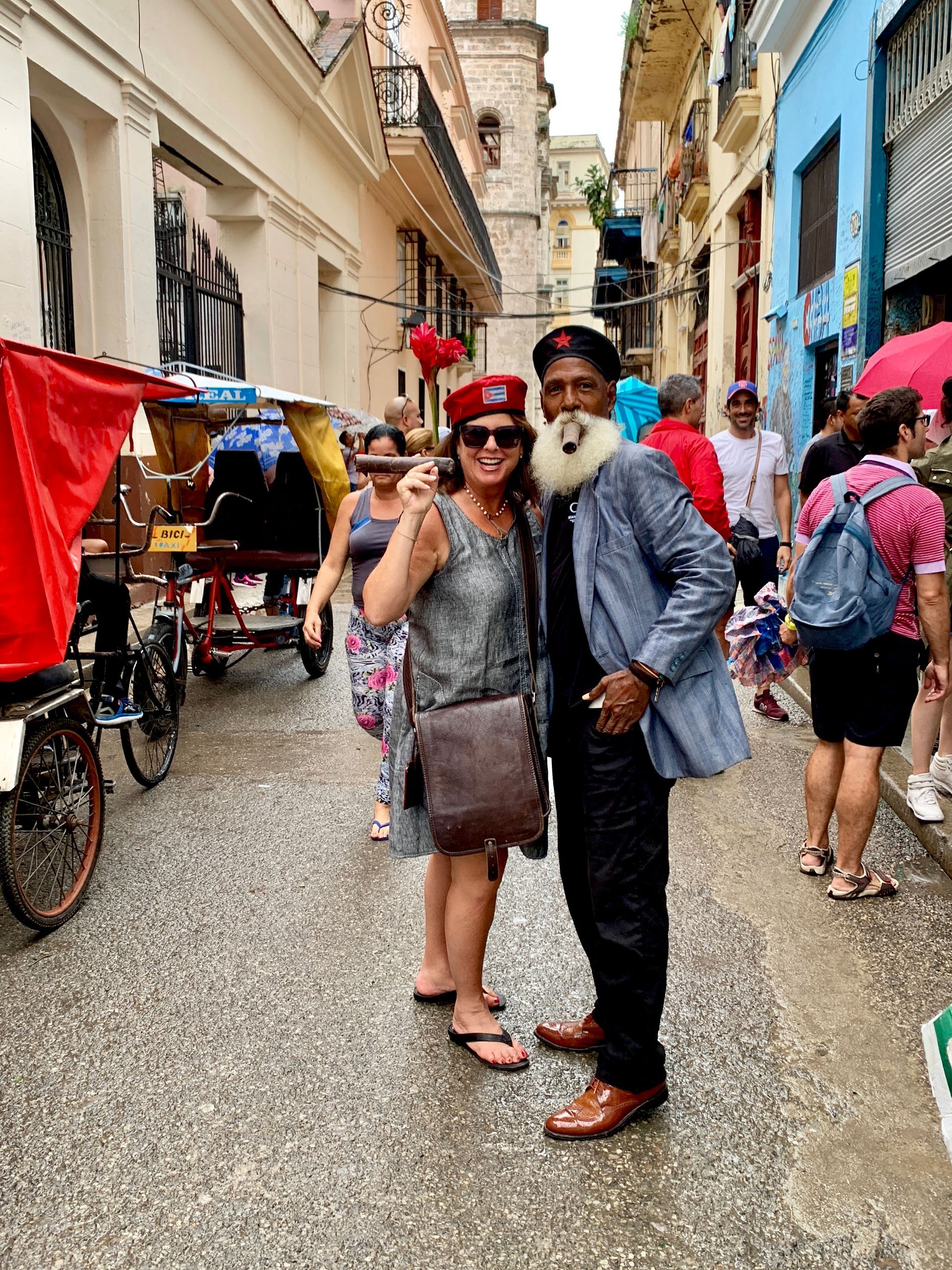 Woman and man pose on a Havana street; woman wears a hat and silver top, man wears a jacket and has a beard.