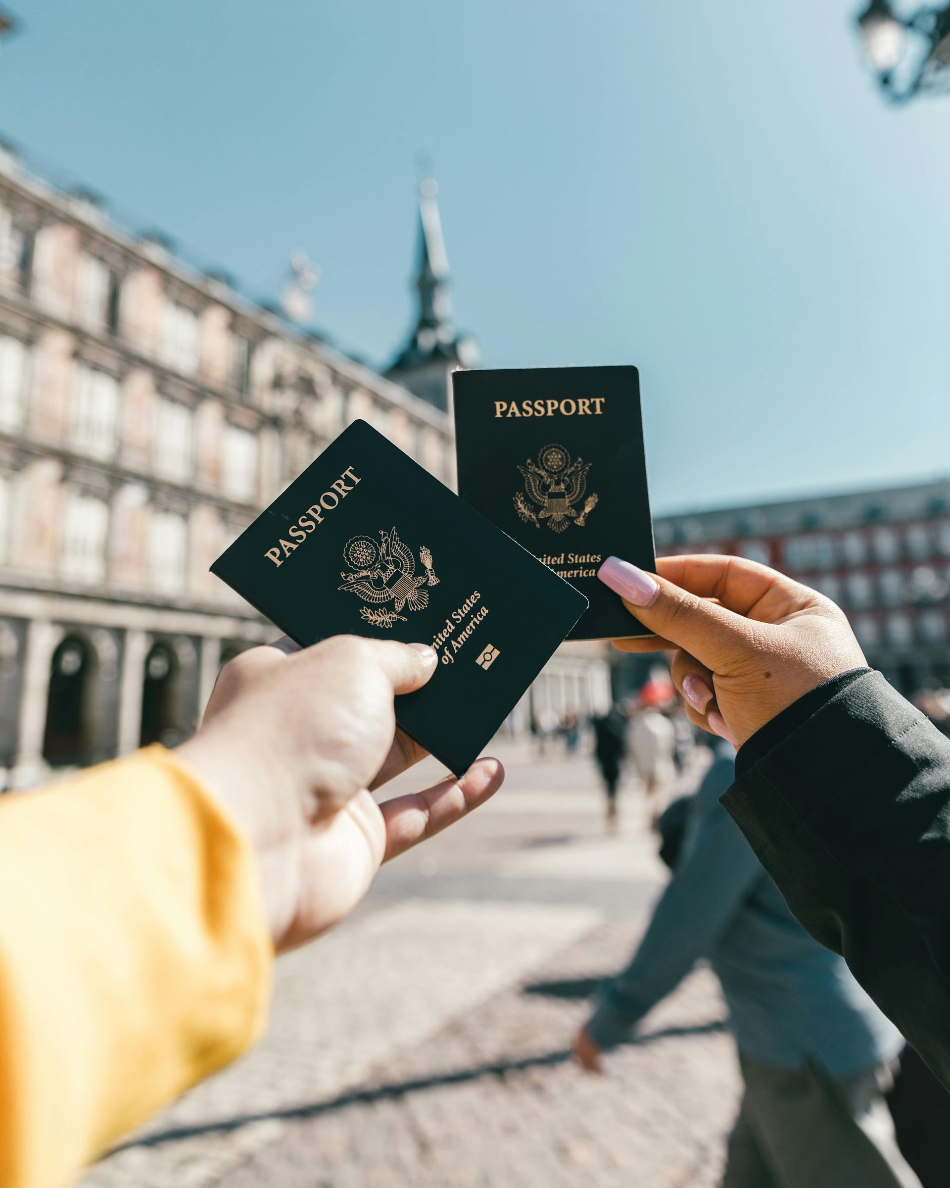 Two people holding up black US passports in a city square.