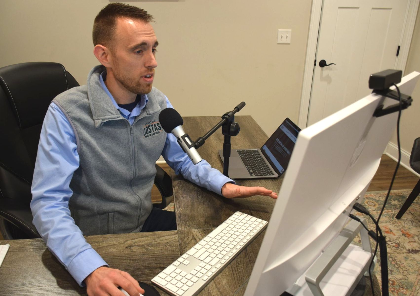 A man is sitting at a desk using a computer and a microphone.