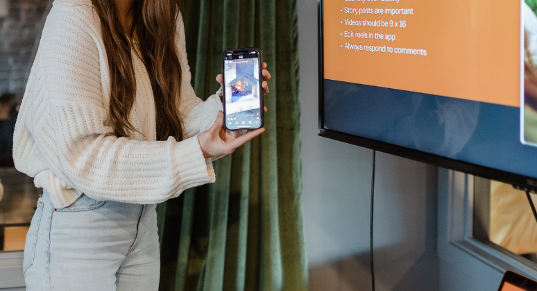 A woman is holding a cell phone in front of a projector screen.